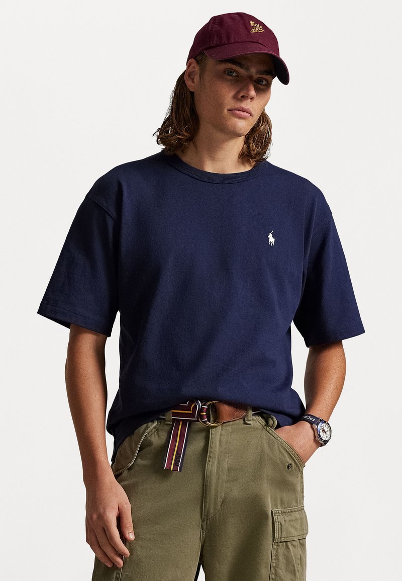 Ναυτικό βαμβακερό μπλουζάκι κοντομάνικο με λαιμ�όκοψη τύπου crew, σε συνδυασμό με ελαιόχρωμα cargo παντελόνια και μπορντώ καπέλο μπέισμπολ.