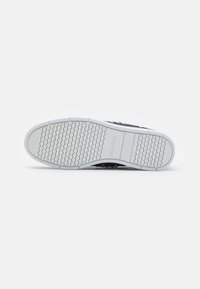 Schwarzer Sneaker mit einer strukturierten Gummisohle, ausgestattet mit einer weißen Laufsohle und dezentem Branding. Das Design weist ein wellenförmiges Muster für besseren Halt auf.