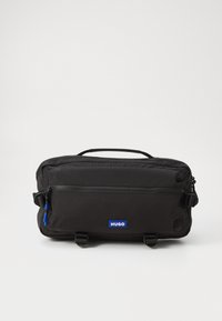 Sort nylon taske med en struktureret overflade, der har et håndtag i toppen, lynlåslukning, frontlomme og blå logoetiket. Kompakt og rektangulært design.