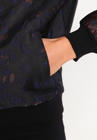 Svart sweatshirt med en strukturerad leoparddesign i mörkblått och koboltackenter. Har ribbade ärmslut och midja.