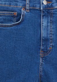 Spijkerbroek in mediumblauw met contrasterende oranje stiknaden. Heeft een ontwerp met vijf zakken, metalen knoopsluiting en zichtbare stikdetails.