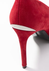 Chaussure à talon haut en daim rouge avec un design épuré. Équipée d'un accent de talon argenté avec "Calvin Klein" gravé. Semelle extérieure noire.