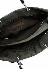 Bolso en verde oliva con herrajes plateados, cierre de cremallera y múltiples bolsillos internos. Cuenta con una etiqueta de cuero cosida en el interior. Textura suave.