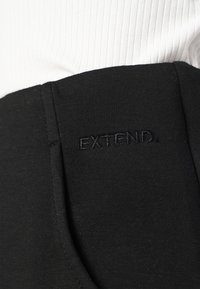 Čierne elastické nohavice s hladkou textúrou, s vysokým pásom a vyšívaným logom "EXTEND" na boku.