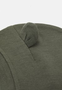 Oliwkowa dzianinowa czapka beanie z zaokrąglonym wierzchołkiem. Posiada mały, złożony akcent oraz gładkie, teksturowane wykończenie. Widoczne detale szwów.