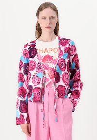 Colorful floral print jacket featuring pink and blue roses on a light background, with a tie front and long sleeves, paired with a graphic t-shirt.
