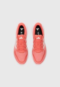 Coral athletic shoes with mesh upper, white three-stripe design, lace-up closure, cushioned midsole, and contrasting black insole.
