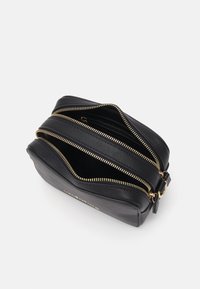 Bolso de cuero negro con dos cremalleras superiores, herrajes dorados, forma estructurada y superficie texturizada. Abierto con compartimentos interiores visibles.