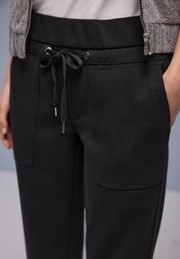 Black jogger pants with a drawstring waist, featuring two front pockets and a textured finish. Straight cut with a mid-rise fit.