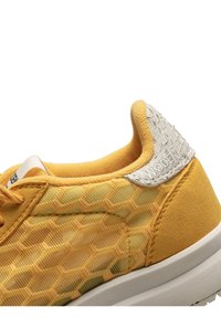 Gelbe Turnschuhe mit einer Wabenstruktur, weichem Stoff und einem strukturierten weißen Absatz. Weiße Außensohle und kontrastierende Nähte.