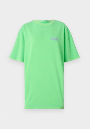 T-shirt en coton vert avec une coupe décontractée, des manches courtes et un col rond côtelé. Il présente un petit texte violet sur la partie gauche de la poitrine.