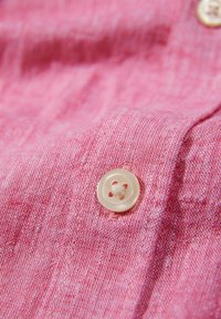 Roze linnen stof met een gestructureerde afwerking, voorzien van een ronde, lichtgekleurde knop met een ontwerp van vier gaten.