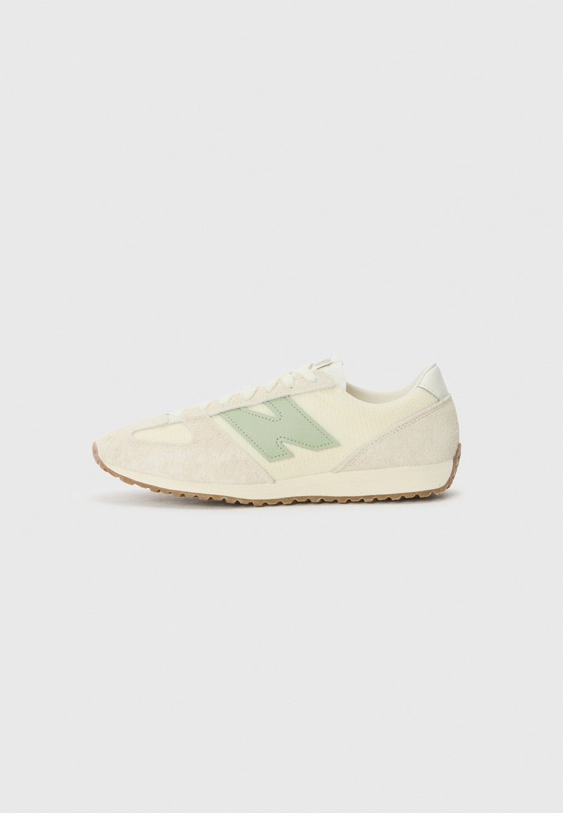 Baskets en daim beige clair et mesh avec un logo "N" vert clair sur le côté et une semelle en gomme, vues de côté sur un fond uni.