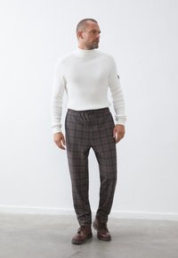 Weißer gerippter Rollkragenpullover, braune karierte Hose mit elastischem Bund, braune Schnürstiefel, mit einer figurbetonten und lockeren Silhouette.