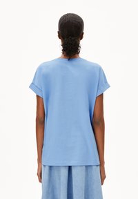 Hellblaues T-Shirt mit kurzen Ärmeln, aus weichem Material, mit lockerer Passform, umgeschlagenen Bündchen und einfachem Design, von hinten gezeigt.
