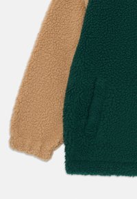 Beige ja tumesinise värviga fliiskanga lähivõte, mis näitab kanga tekstuurset, pehmet ja lokkis pinna detaili rõivas.