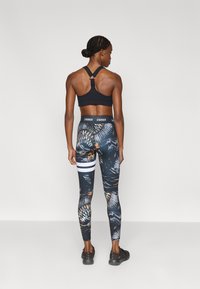 Μαύρο αθλητικό σουτιέν με σχεδιασμό racerback, σε συνδυασμό με σχέδιο κολάν με μαύρη βάση, πορτοκαλί λεπτομέρειες και λευκές ρίγες στη μέση.