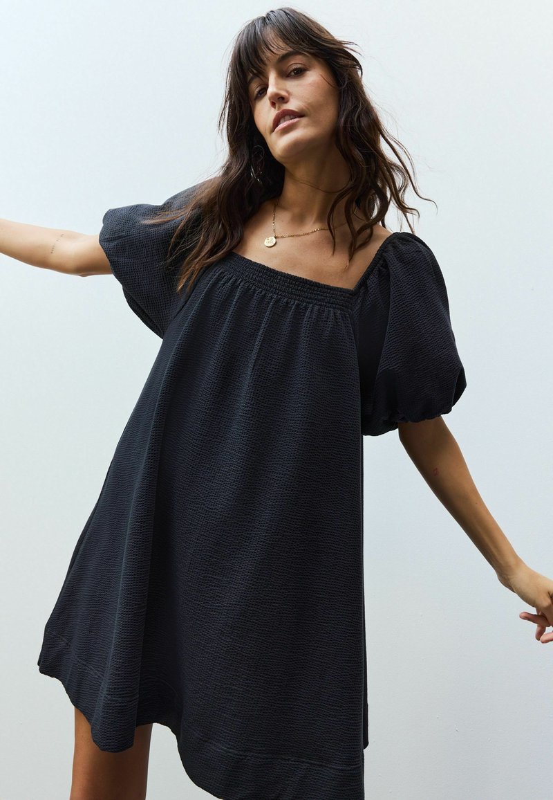 Zwarte jurk met korte mouwen, een vierkante halslijn en gathered textuur. Heeft een losse pasvorm en een asymmetrische zoom.