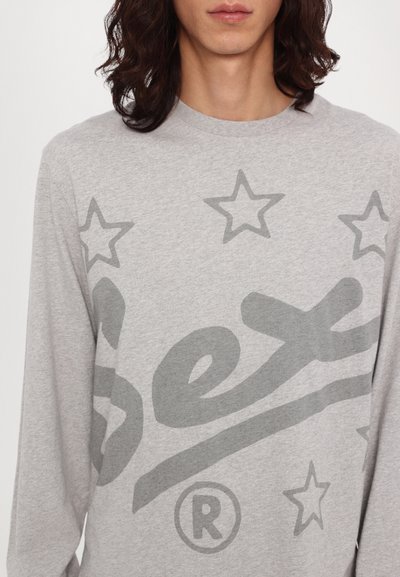 Long-sleeve gray T-shirt made of cotton, featuring large, faded black text and star patterns in varying sizes across the chest.