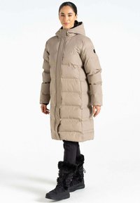 Beige Daunenjacke mit Kapuze, mit gestepptem Muster und Reißverschluss vorne. Kombiniert mit schwarzen Hosen und winterlichen Stiefeln mit Fellbesatz.