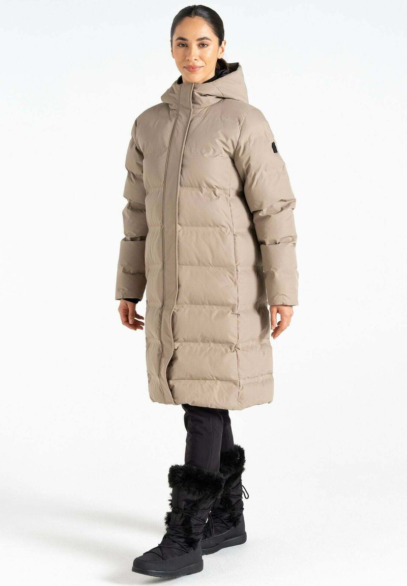 Beige Daunenjacke mit Kapuze, mit gestepptem Muster und Reißverschluss vorne. Kombiniert mit schwarzen Hosen und winterlichen Stiefeln mit Fellbesatz.