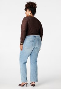 Lichtblauwe rechte jeans met een ontspannen pasvorm, voorzien van achterzakken en een subtiele wassing. Draagt een bruine top met structuur en schoenen met hak.