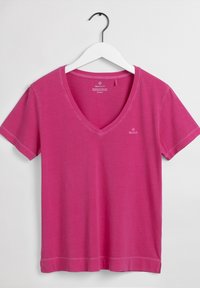 Różowa bawełniana koszulka V-neck z krótkimi rękawami. Posiada dołek z bocznymi rozcięciami oraz małe logo na piersi. Gładka tekstura.