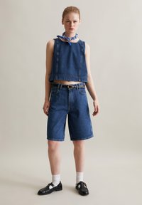 Dżinsowy crop top o kwadratowym wzorze, w zestawie z dżinsowymi szortami do kolan. Stylizacja zawiera niebieski wzorzysty szalik oraz czarne buty ze skarpetkami.