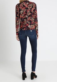 Maglietta a maniche lunghe con base nera e un motivo floreale colorato, abbinata a jeans skinny blu scuro e scarpe col tacco nere.