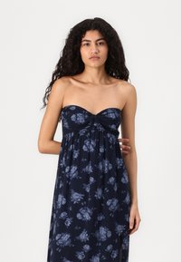 Navy floral maxi dress with strapless design, twisted front detail, and flowing fabric featuring large blue-gray flower patterns.
