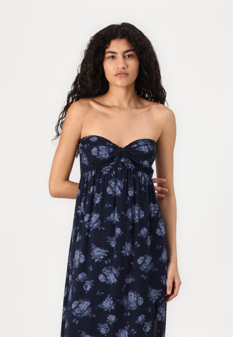 Maritimer Blümchen-Maxikleid mit trägerlosem Design, gedrehtem Frontdetail und fließendem Stoff mit großen blau-grauen Blumenmustern.