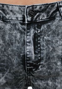 Jeans in denim nero con una texture sfumata e marmorizzata, dotati di chiusura frontale a bottone e passanti per cintura, mostrati dalla prospettiva della vita.