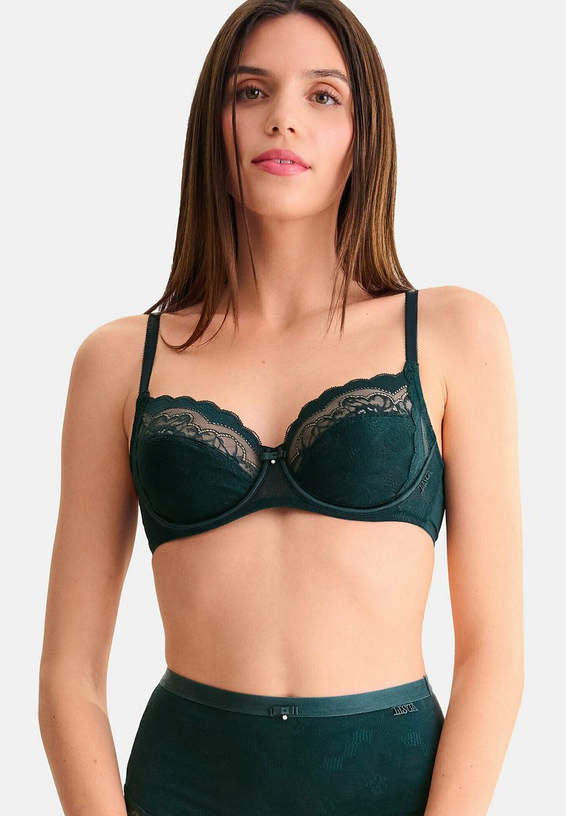 Soutien-gorge en dentelle vert foncé avec des bords festonnés, un maintien par armatures, des bretelles réglables, et un détail décoratif à l'avant. Fini satiné lisse.