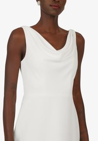 Weißes Kleid mit Cowl-Neck, das eine glatte Textur, ein ärmelloses Design und eine figurbetonte Silhouette aufweist. Dezente Nähedetails entlang der Taille.