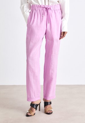 Pantalons en lin rose clair avec une taille élastique, fermeture à cordon de serrage, poches latérales et coupe décontractée. Associés à des sandales à talons noires et beiges.