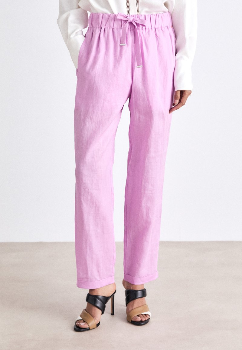 Pantalons en lin rose clair avec une taille élastique, fermeture à cordon de serrage, poches latérales et coupe décontractée. Associés à des sandales à talons noires et beiges.
