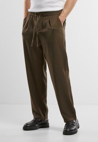 Pantalons légers marron avec une taille élastique et un cordon de serrage, dotés de poches latérales, d'un design à jambe droite et d'une texture lisse.