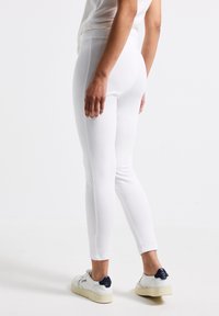 Leggings blancs avec une texture lisse et une coupe ajustée, dotés d'une taille haute et d'une coupe longueur cheville, associés à des baskets blanches.