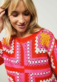 Kleurrijke gehaakte trui in levendig rood, roze, oranje en wit. Heeft geometrische patronen met open steken en textuuraccenten.