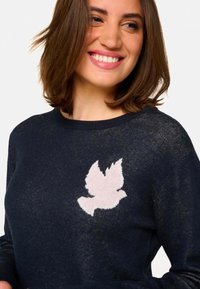 Pull en maille bleu marine avec un emblème de oiseau rose clair texturé sur la poitrine, doté d'un col rond et d'une coupe décontractée.