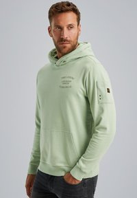 Sudadera verde clara hecha de tela suave, con un bolsillo frontal, capucha ajustable con cordones y un bolsillo en la manga con acento de marca.