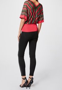 Kaksivärinen toppi, jossa on pystysuoria raitoja vihreänä ja punaisena, yhdistettynä mustiin kapeisiin farkkuihin, joissa on valkoiset sivusaumat ja korkokenkiin.