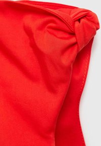 Roter Stoff mit glatter Textur und leichtem Glanz, der oben ein geknotetes Design und saubere genähte Ränder aufweist.