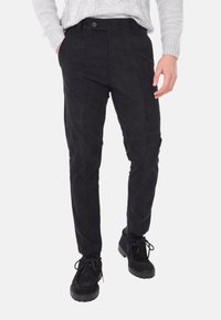 Pantaloni in corduroy neri con vestibilità slim, dotati di tasche visibili e chiusura frontale con bottone. Il tessuto testurizzato aggiunge profondità al design.