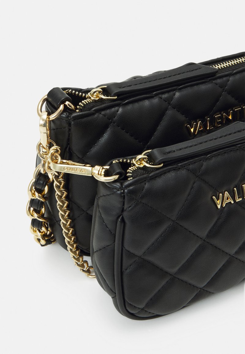 Schwarze, gesteppte Lederhandtasche mit einem goldenen Kettenriemen und Hardware, die über zwei Reißverschlussfächer und geprägte Logoakzente verfügt.