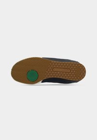 Semelle de basket Lacoste avec une semelle extérieure en caoutchouc gomme à motif texturé, un accent circulaire vert et une tige en matériau bleu foncé.