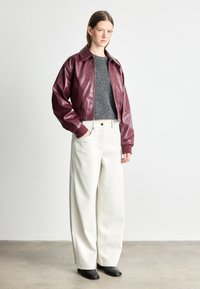 Μπορντό δερμάτινο κοντό μπουφάν με γιακά, συνδυασμένο με γκρι πουλόβερ και κρεμ παντελόνι με φαρδιά πόδια. Μαύρες μπότες με τακούνι ολοκληρώνουν το σύνολο.