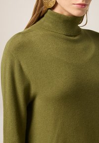 Maglione a collo alto verde oliva realizzato in tessuto morbido, caratterizzato da un collo aderente e una texture sottile, che mette in risalto il design pulito.