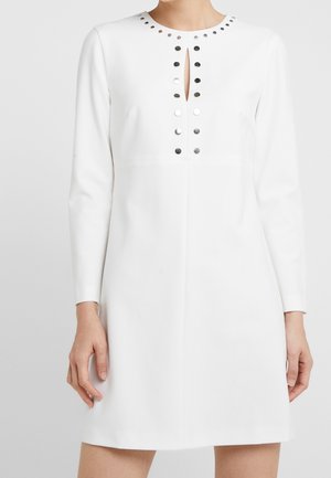 Robe blanche à manches longues avec un col rond, ornée d'empiècements métalliques argentés sur le devant et d'une petite ouverture en forme de clé. Texture lisse.