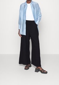 Chemise en satin bleu clair, haut blanc à col rond, pantalons noirs à jambe large avec cordon de serrage, et sandales noires épaisses avec des brides.